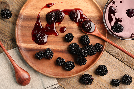 Tasty blackberry jam and fresh berries on wooden table, flat lay