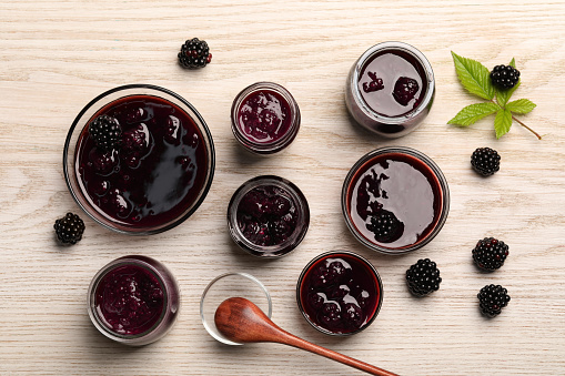 Tasty blackberry jam and fresh berries on white wooden table, flat lay