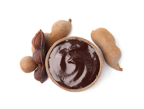 Bowl of tamarind sauce and fresh pods isolated on white, top view