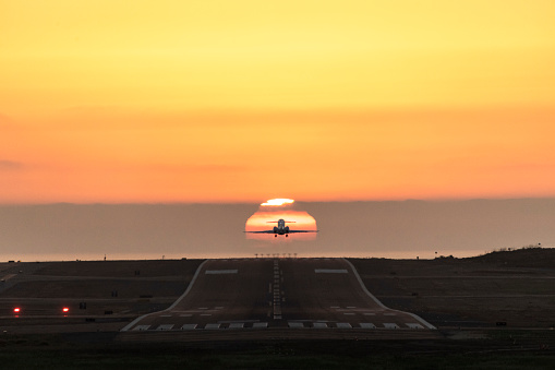 Small airplane taking off at sunset, flying into the sun.
