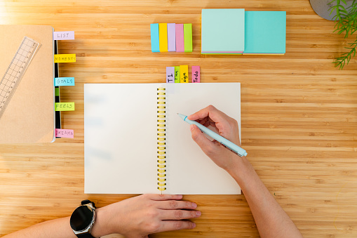 woman writing appointments in a diary organizer  with a lot of colorful sticky notes and maker management on the desk at home.