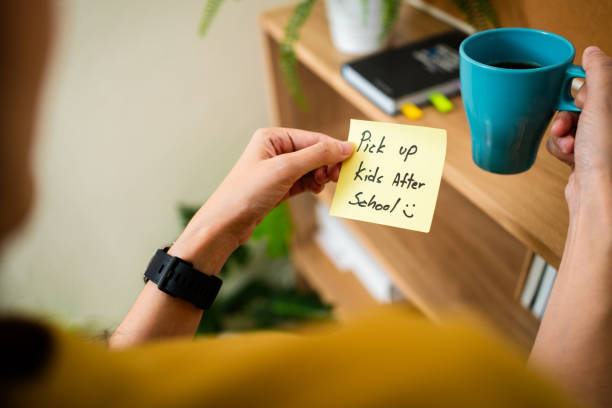 istock Woman looking on a sticky note reminder to pick up kid from school. 1927678325
