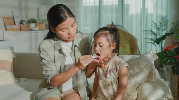 Mom takes Care of her daughter who gets sick and has a high fever, cold, and flu, and feeds medicine to her child at home. Illness Girl with a medical condition and family wellness. Mom takes Care of her daughter who gets sick and has a high fever, cold, and flu, and feeds medicine to her child at home. Illness Girl with a medical condition and family wellness concept. child liquid medicine stock pictures, royalty-free photos & images