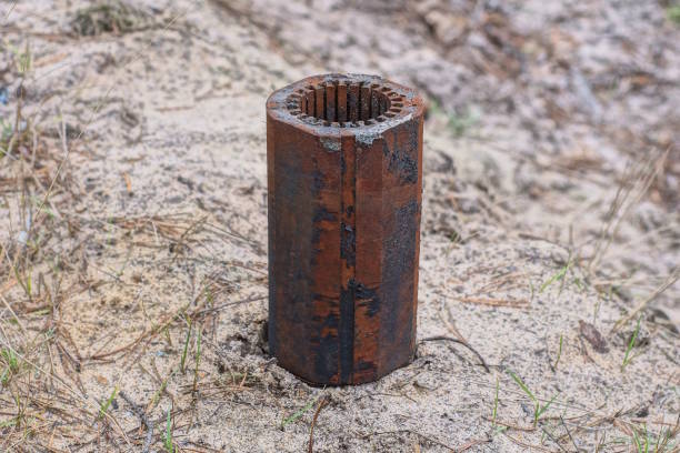 one large rusty brown piece of pipe standing on the gray sand on the street