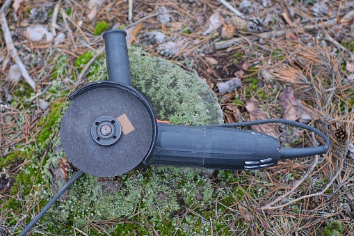 Una herramienta eléctrica de una amoladora negra yace en el musgo verde photo