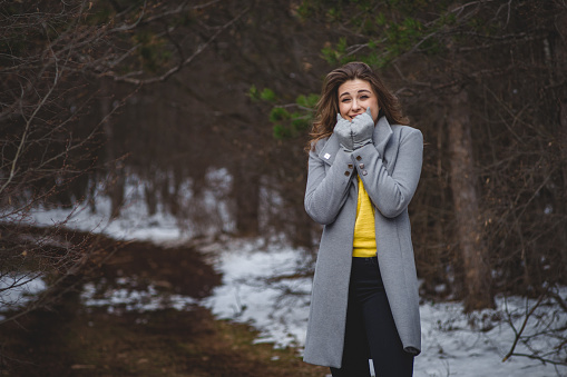Young woman trying to warm up her frozen hands with breath outdoor in winter time
