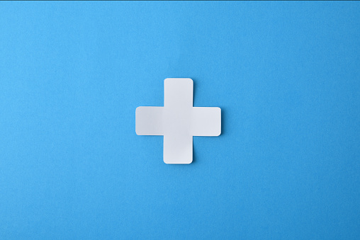 Conceptual medicine symbol with cross shaped paper cutout isolated in the center on blue background.