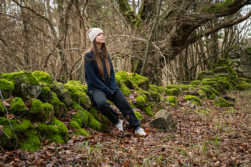 A white woman, with brown hair and a veis hat, in an Irish forest with green and brown tones through the trees