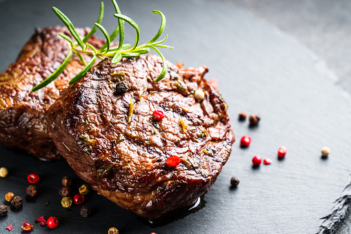 Meat steaks. Beef medallions with spices and herbs at stone board on black background.