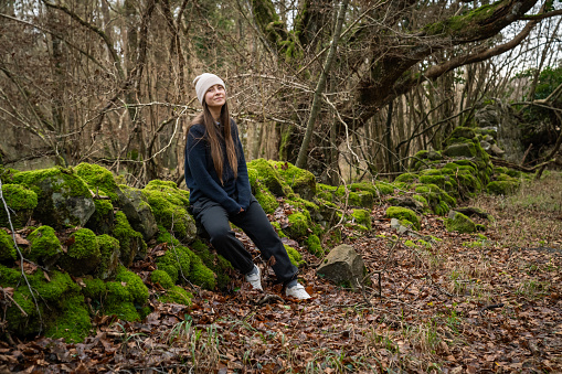 A white woman, with brown hair and a veis hat, in an Irish forest with green and brown tones through the trees