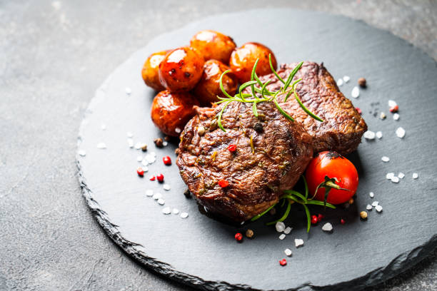 istock Meat steaks with vegetables and herbs at black board. 1927748769