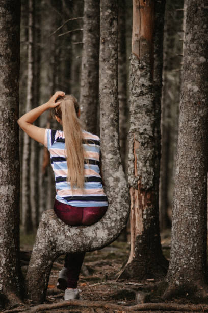 istock Young woman sitting on tree trunk in pine forest 1927748791