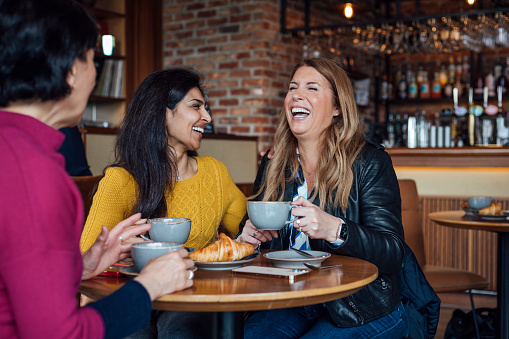 Close up of three mature women sitting side by side in a cafe in Newcastle, England. They are enjoying breakfast and hot drinks in the morning while one woman is using her smartphone to show her friend something. They are on a friends reunion city break for the weekend.