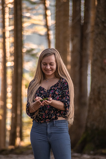 Happy young woman holding moss in her hands and showing it in a forest