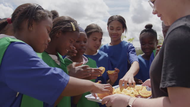 Coach hold a tray of refreshing orange slices for girls playing sport together