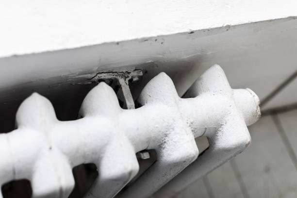 Old fashioned radiator on white wall near the window
