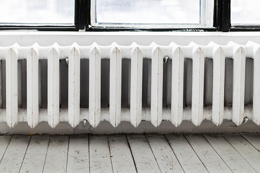 Old fashioned radiator on white wall near the window