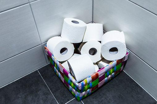 A pile of toilet rolls in a colourful basket in the corner of a toilet