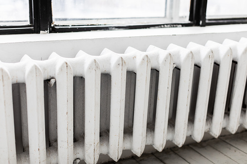 Old fashioned radiator on white wall near the window