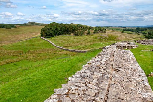An image of Hadrian's Wall, a historic fortification in Northern England. This ancient structure, stretching across the rugged landscape, stands as a testament to Roman engineering and a poignant reminder of the past, weaving through the rolling hills and green fields of the English countryside.