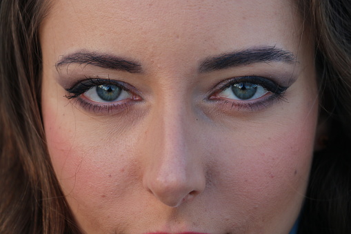 A closeup of a blue eyed Ukrainian woman's face. She has makeup, brown hair and blue eyes.