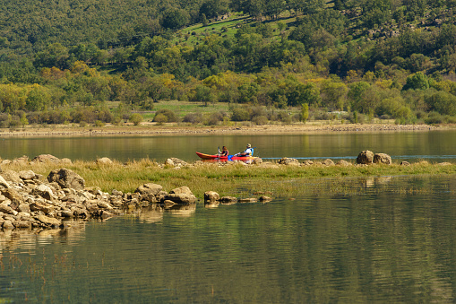 Lozoya, Madrid; 2023 October - 07: Tourists are seen in the distance in their leisure canoe on a sunny day at the Pinilla reservoir. Picturesque and dreamlike landscape.
