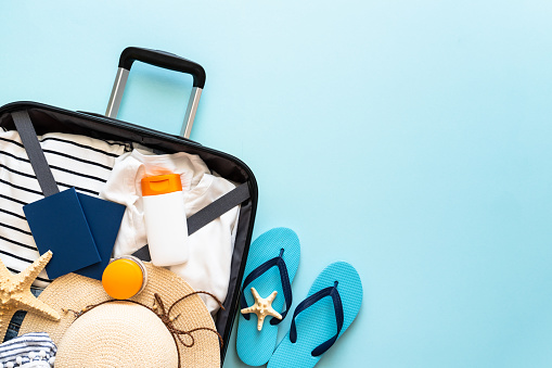 Open Suitcase with summer cloth, hat, passports and flip flops on blue background. Happy Holidays, travel concept. Flat lay image.