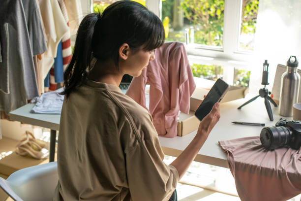 istock Entrepreneur young Asian woman immersed in her side hustle, using a mobile app, selling trendy fashion clothes from the comfort of her home. dedication to building a business and creating stylish online shopping in her free time, Side hustle concept 1927863696