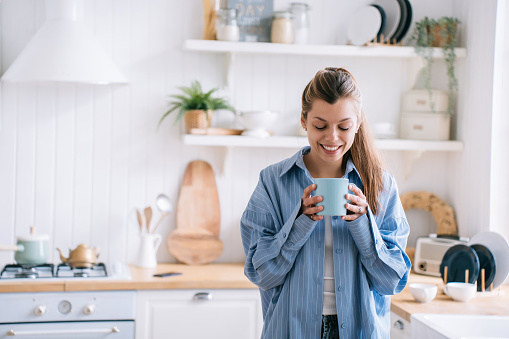 Smiling woman enjoying a cup of coffee in a bright, cozy kitchen, evoking warmth and comfort