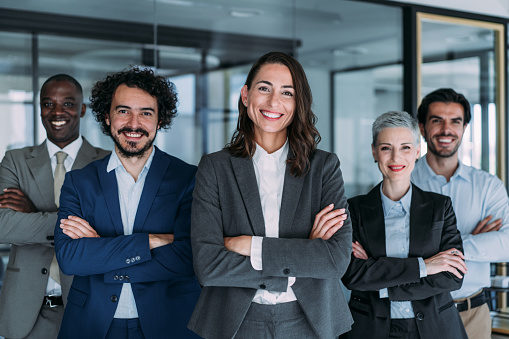 Portrait of beautiful smiling businesswoman with her colleagues. Multi-ethnic group of business persons standing in modern office. Successful team leader and her team in background.