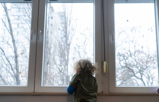 istock Little boy with plaster cast at home looking through window 1927881813