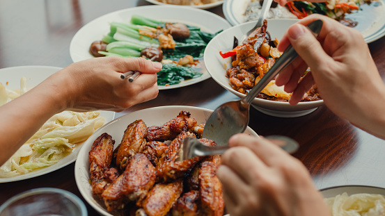 Closeup of young Asian family eating food and having fun sitting at dining table at backyard outside home. Multi-generation family enjoying spending together concept.