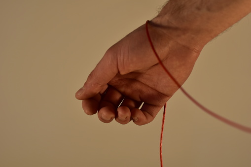 Hand holding red string. Human hand on a white background holding piece of red string or rope