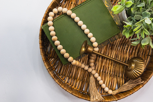 Flat lay on white wood table top with wicker tray, old books, wood beads, gold candle holder and small plant with copy space