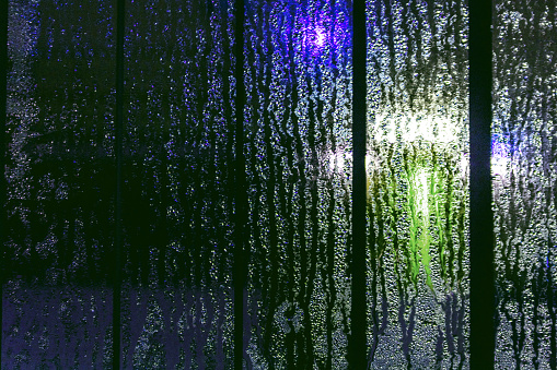 Light through raindrops on glass, abstract background of a city street in bokeh.