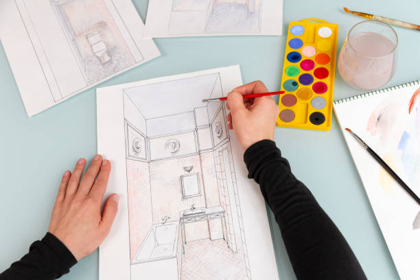 istock Close up interior designer's hands, which are working on color hand drawing of bathroom using watercolor paints and brush 1928013131