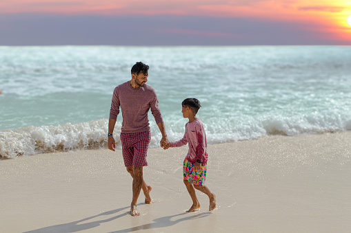 A parent and child walk across a beach, under a sunset.
