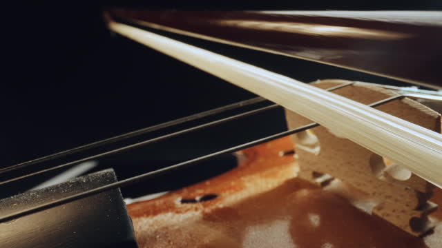 Master artisan luthier or violinist playing with bow on handmade quality wooden violin or cello, macro slow motion shot