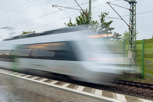 Photo of train in blurred motion outdoors. Photography with long exposure. Transport concept, traveling picture with high speed vehicle. Rainy weather, railway station.