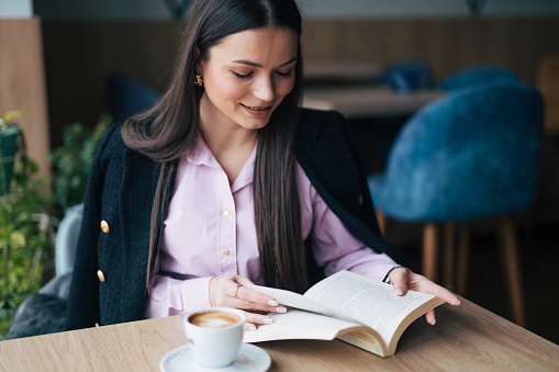 Attractive young woman reading a book while drinking coffee