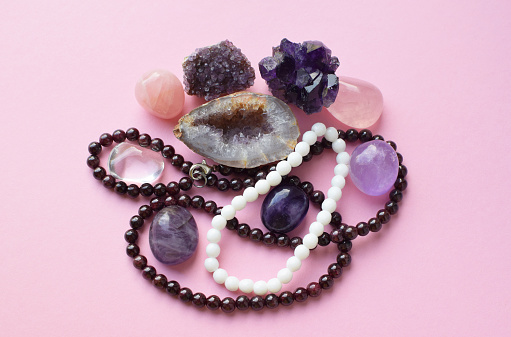 Garnet beads and amethyst, rose quartz and rock crystal crystals on a pink background.