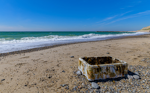 Fish crate from the fishing industry, covered with algae, lies on the beach. Waves carried a plastic container from the fishery and leave it stranded at the water's edge.Plastic waste on the beach.