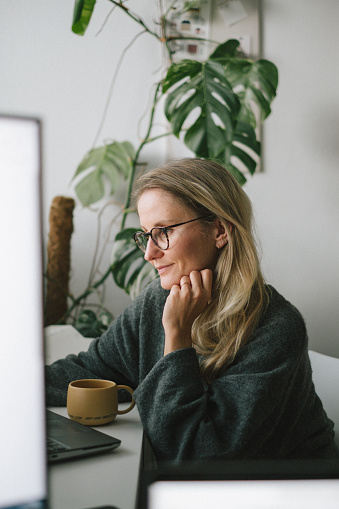 Young woman works on computer at home, drinks hot beverage