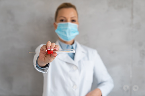 A nurse in a white coat and a face mask is holding a swab tube.