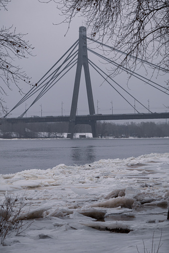 Kyiv, Ukraine - January 11, 2024. Outside, the temperature is sub-zero and frosty. A beautiful bridge can be seen behind. Light snow falls and sprinkles the city. A little fog begins and the sky is very gray.