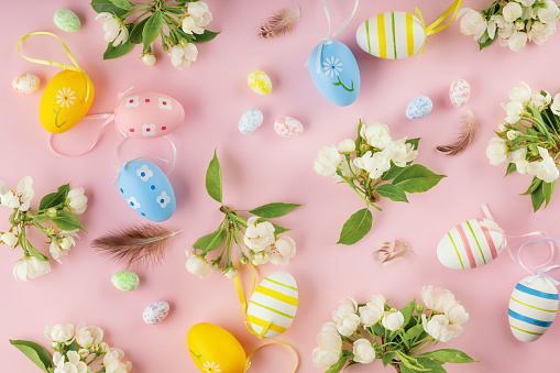 Happy Easter greeting card. Easter eggs, blooming apple flowers on pastel pink background. Easter and spring concept. Flat lay, top view.