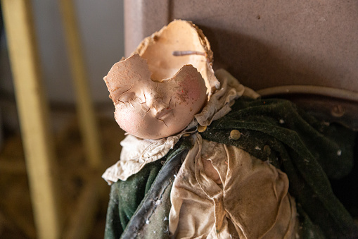 An old broken antique doll sitting in a chair