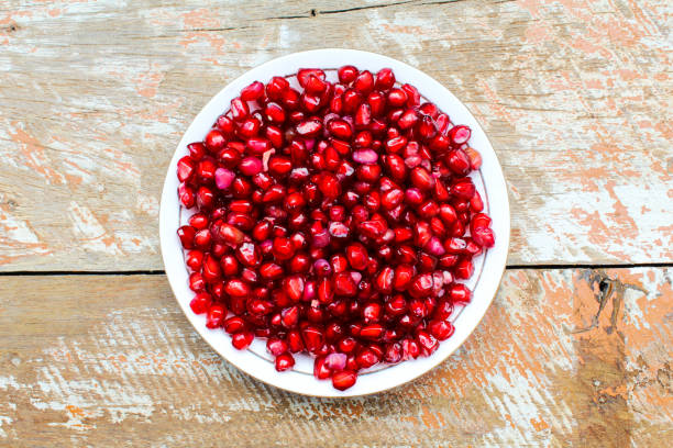 Pomegranate seeds in a plate on wooden background top view