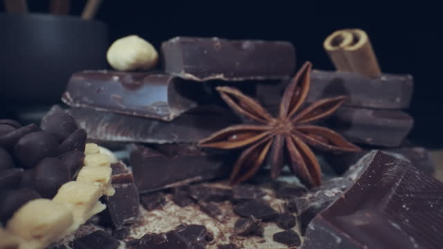Macro cozy scene of various chocolate with cinnamon sticks, chocolate pieces on a wooden table, hazelnuts and dried anise star