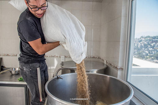 man with sack of barley pouring the seeds into pot of boiling water for craft beer production